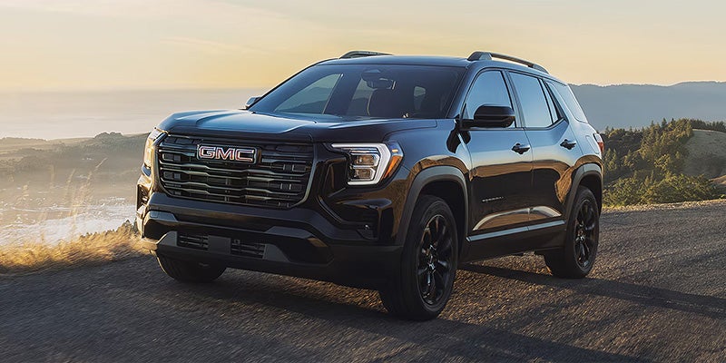 Black GMC Terrain parked on a scenic road overlooking a coastal landscape at sunset